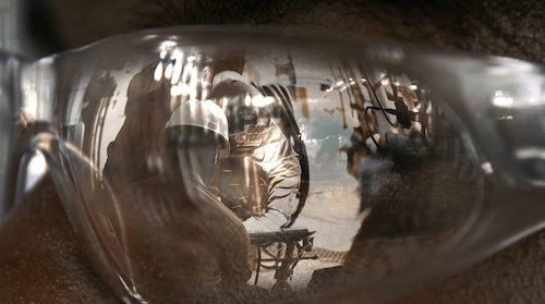 A reflection in safety glasses depicts a construction crew