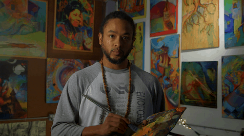 An African American artist dips his brush into orange paint