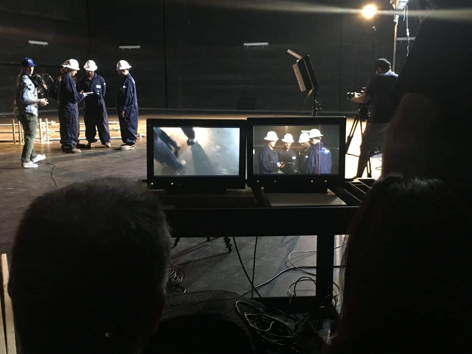A production team films three actors dressed in construction uniform gear