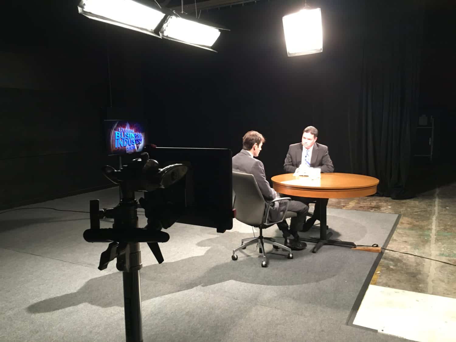 A newsman interviews a businessman in a dark studio