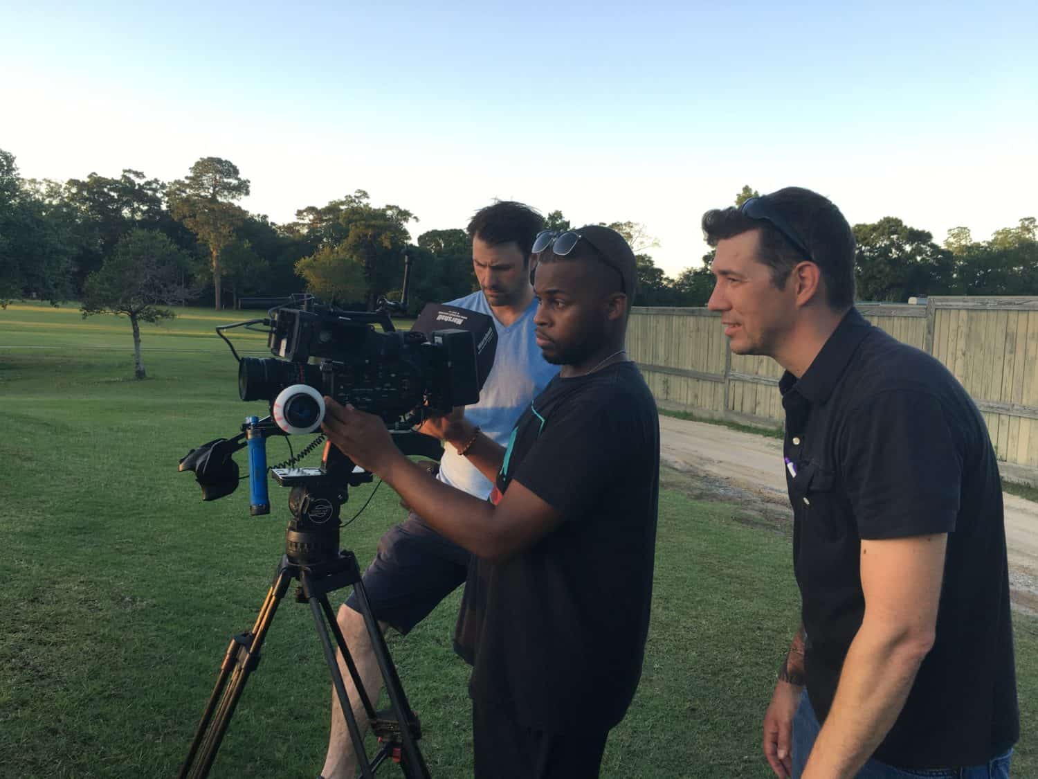 Three camera men talk about camera angles in a park on a sunny day