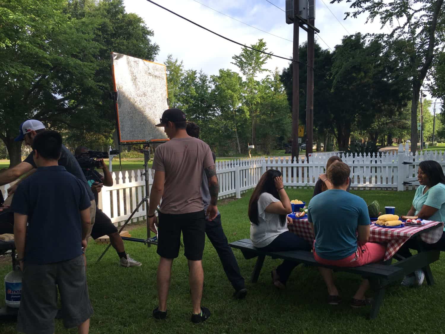 A camera crew films a group of friends eating a picnic