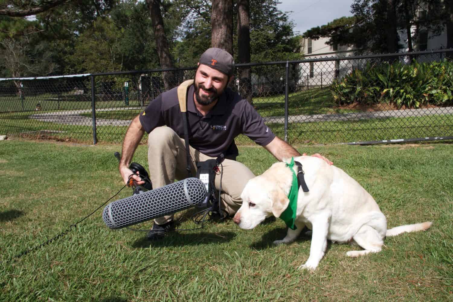 A camera man pets a golden retriever in a park
