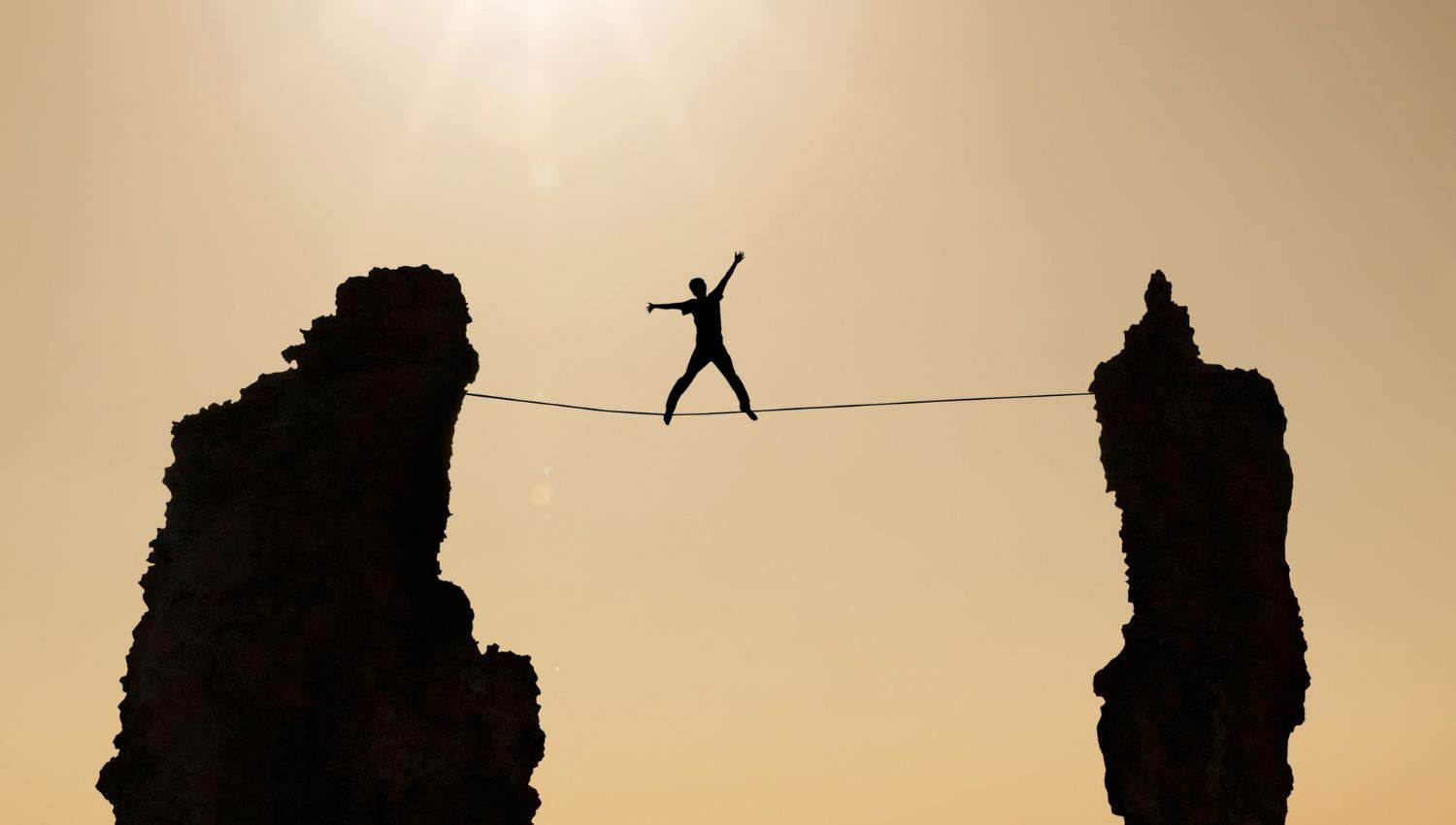 A man walks across a tight rope suspended between two tall rock formations