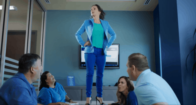 Woman in a blue suit stands on a conference desk in Assurance FInancial