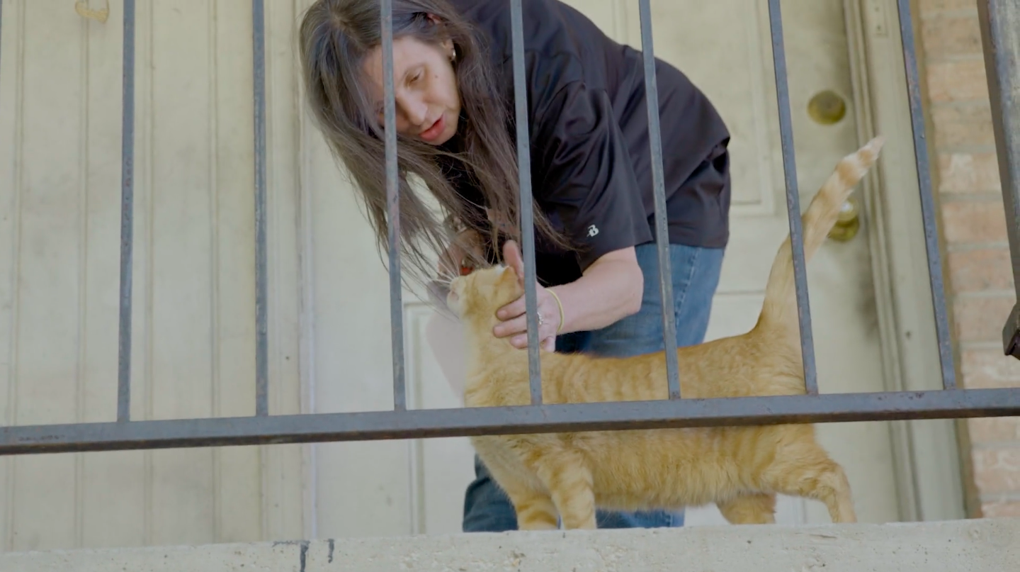 Caucasian woman pets an orange cat on a porch